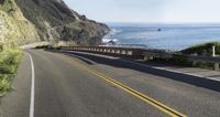 the road is winding by the side of the ocean and there are yellow lines on it