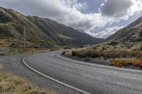 the winding road is surrounded by mountains and scrubby land with sparse bushes and green grass