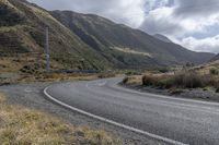 the winding road is surrounded by mountains and scrubby land with sparse bushes and green grass