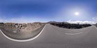 a view of a winding road in front of mountains and a bright sun behind it