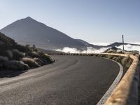 a winding winding road in front of an volcano on a sunny day with low clouds