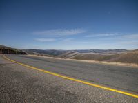 the road winds up a slope near mountains in this area with a sky view of rolling hills and mountains