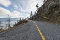 the winding road is empty and empty on both sides of the cliff, while a yellow warning sign marks the side