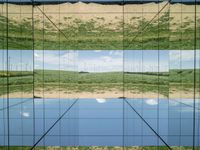 large glass cube reflecting water and grass with mountains in the distance near it, on the floor of square open area