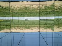 large glass cube reflecting water and grass with mountains in the distance near it, on the floor of square open area