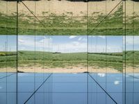 large glass cube reflecting water and grass with mountains in the distance near it, on the floor of square open area