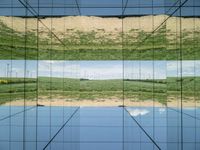 large glass cube reflecting water and grass with mountains in the distance near it, on the floor of square open area