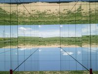 large glass cube reflecting water and grass with mountains in the distance near it, on the floor of square open area