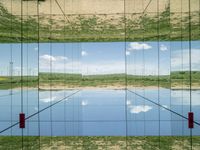 large glass cube reflecting water and grass with mountains in the distance near it, on the floor of square open area