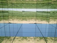 large glass cube reflecting water and grass with mountains in the distance near it, on the floor of square open area