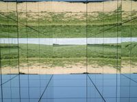 large glass cube reflecting water and grass with mountains in the distance near it, on the floor of square open area