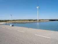 the road is empty and clear of people standing on the curb near the water and wind turbines