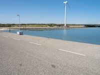 the road is empty and clear of people standing on the curb near the water and wind turbines