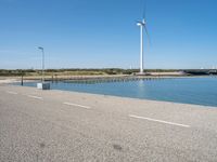 the road is empty and clear of people standing on the curb near the water and wind turbines