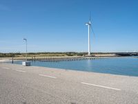 the road is empty and clear of people standing on the curb near the water and wind turbines