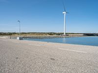 the road is empty and clear of people standing on the curb near the water and wind turbines