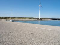 the road is empty and clear of people standing on the curb near the water and wind turbines