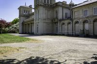 the two story castle sits in a field with green grass and trees, which are beside its gated area