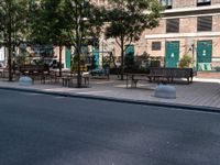 empty sidewalk with tables and benches outside on sunny day near building with tree and bench area