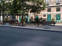 empty sidewalk with tables and benches outside on sunny day near building with tree and bench area