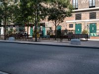 empty sidewalk with tables and benches outside on sunny day near building with tree and bench area