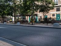 empty sidewalk with tables and benches outside on sunny day near building with tree and bench area