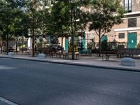 empty sidewalk with tables and benches outside on sunny day near building with tree and bench area