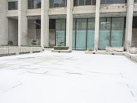 a person in red jacket walking with umbrella through snow covered courtyard area near building with large windows and walkway