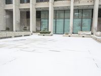 a person in red jacket walking with umbrella through snow covered courtyard area near building with large windows and walkway