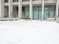 a person in red jacket walking with umbrella through snow covered courtyard area near building with large windows and walkway