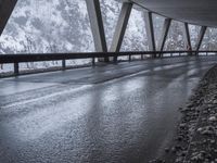 snow covered mountain side on the road with an empty wet road under it and mountains in the background