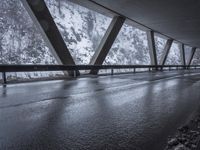 snow covered mountain side on the road with an empty wet road under it and mountains in the background