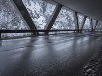 snow covered mountain side on the road with an empty wet road under it and mountains in the background