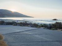 a parking lot with sand and hills in the background and the sun setting over a beach