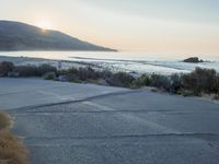 a parking lot with sand and hills in the background and the sun setting over a beach