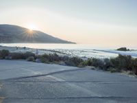 a parking lot with sand and hills in the background and the sun setting over a beach