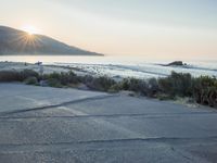 a parking lot with sand and hills in the background and the sun setting over a beach