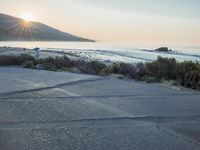 a parking lot with sand and hills in the background and the sun setting over a beach