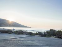 a parking lot with sand and hills in the background and the sun setting over a beach