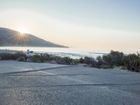 a parking lot with sand and hills in the background and the sun setting over a beach