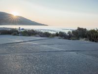 a parking lot with sand and hills in the background and the sun setting over a beach