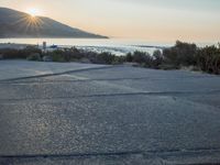a parking lot with sand and hills in the background and the sun setting over a beach