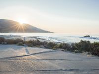 a parking lot with sand and hills in the background and the sun setting over a beach