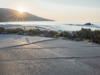 a parking lot with sand and hills in the background and the sun setting over a beach