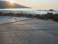 a parking lot with sand and hills in the background and the sun setting over a beach