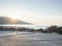 a parking lot with sand and hills in the background and the sun setting over a beach