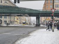 a green bridge spanning over a snowy city street next to buildings and street lights filled with snow