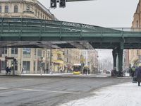 a green bridge spanning over a snowy city street next to buildings and street lights filled with snow