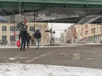 people are walking across the snow with an umbrella under a bridge in a city street