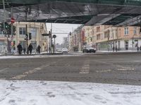 people cross the snow covered street under a bridge and overpass as they walk in the foreground